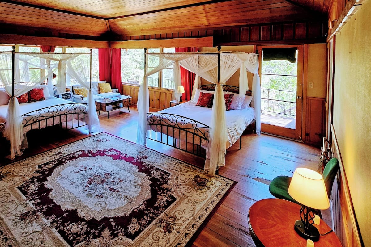 A spacious bedroom with two beds, a large ornate rug, and a view of the outdoors.