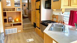 Cocina compacta para vehículos recreativos, con armarios de madera, estufa, fregadero y microondas.