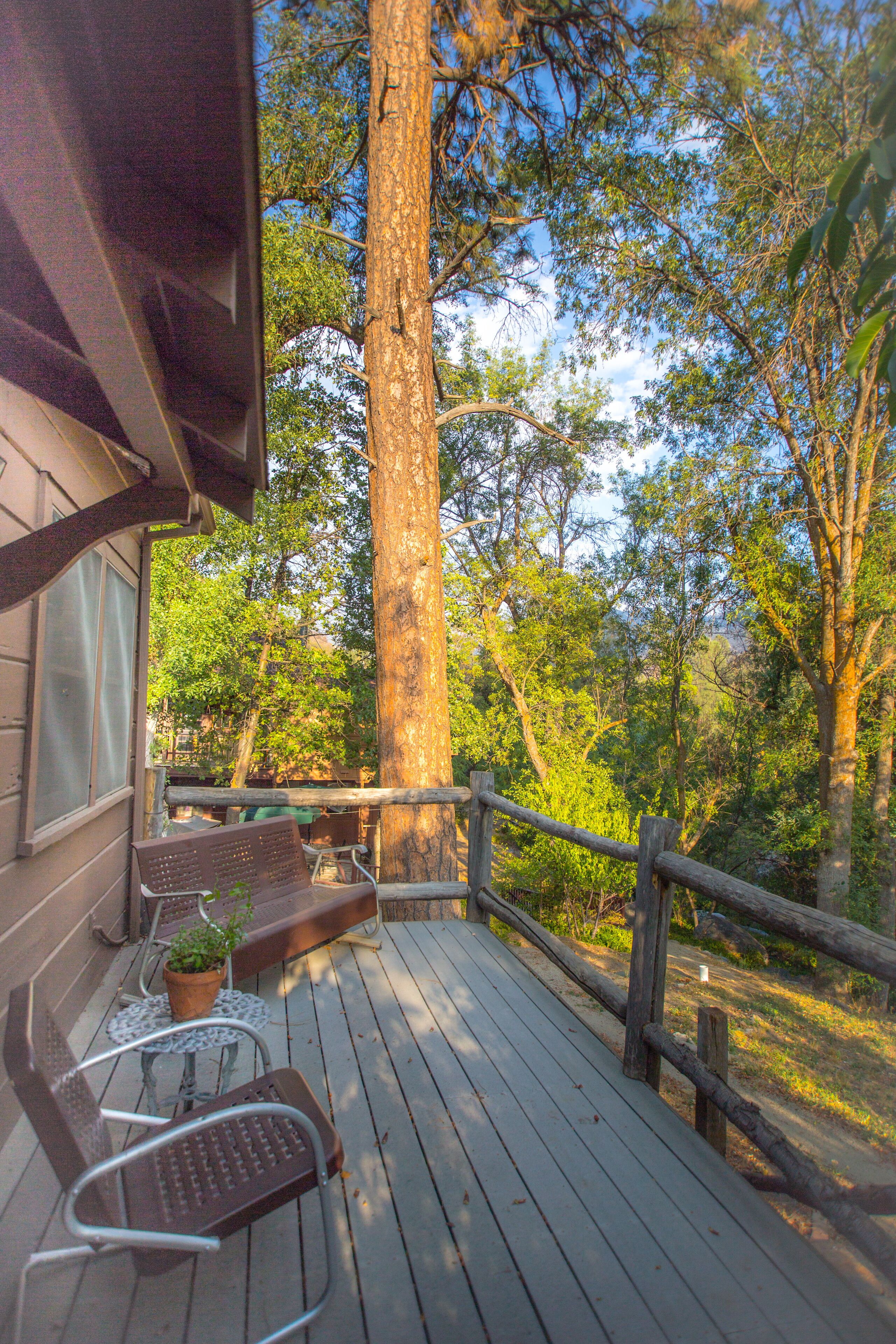 A wooden deck with two metal chairs and a bench, overlooking a forested area.