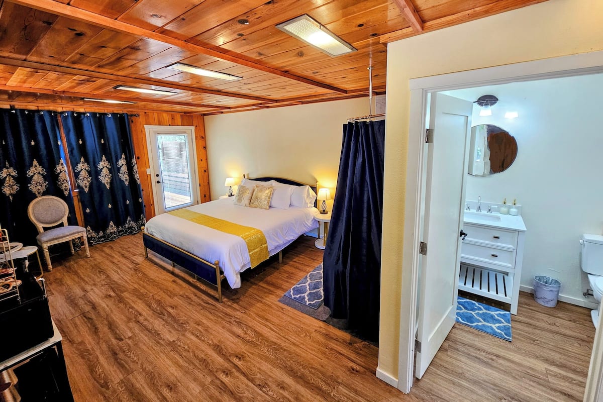 A bedroom with a wooden ceiling, a bed with white bedding, a nightstand, a chair, and a desk with a computer.