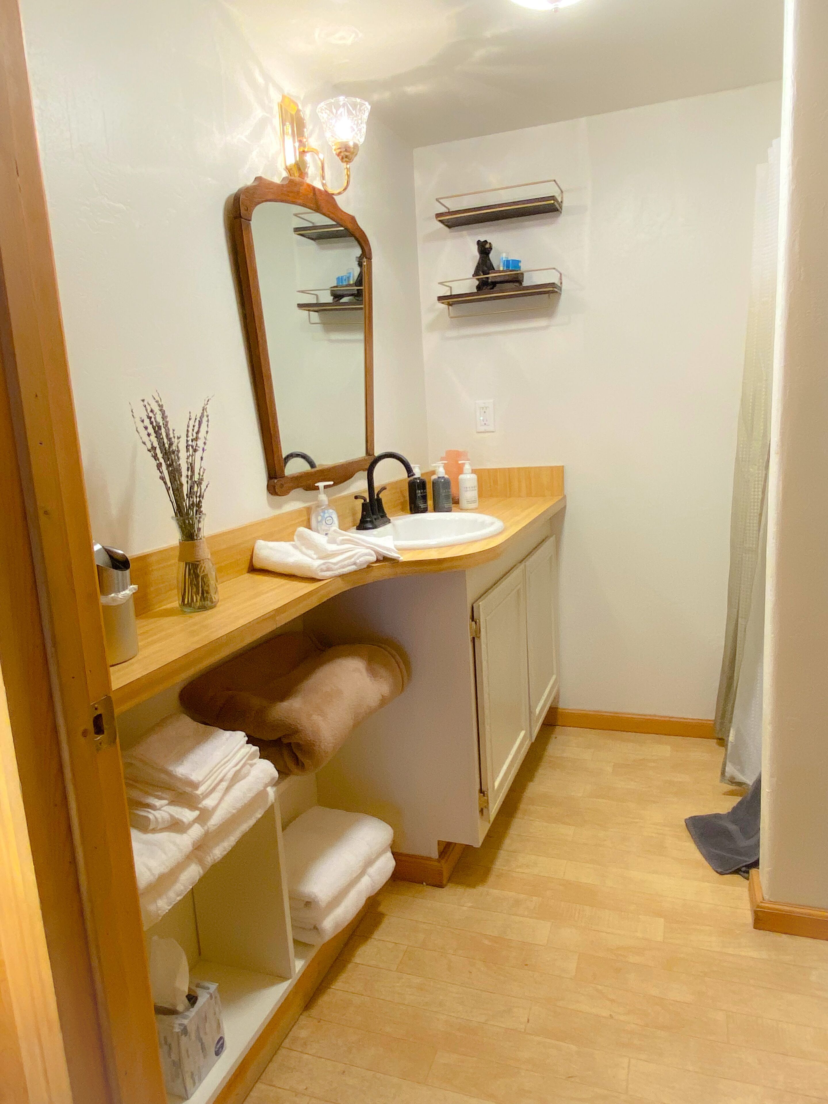 Un baño pequeño con tocador de madera, un espejo, un lavamanos y un estante con artículos de aseo.
