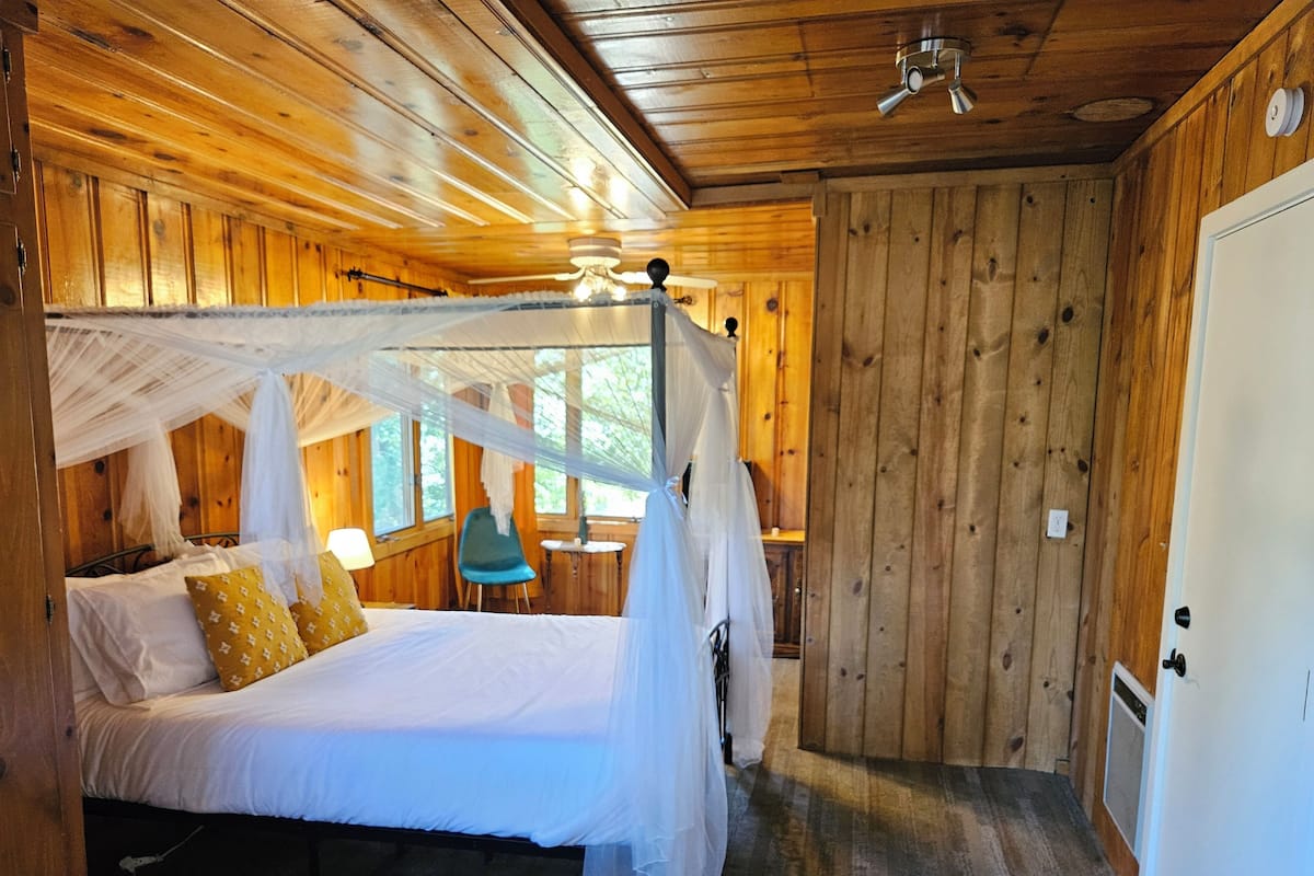 A wooden cabin bedroom with a canopy bed, a small table, and a chair.