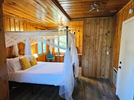 Quarto de cabana de madeira com cama de dossel, uma mesa pequena e uma cadeira.