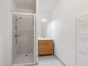 A modern bathroom with a glass shower enclosure, a wooden vanity with a mirror, and a white tiled floor. - Appartement Conquistar - Welkeys (Cabourg)