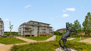 A modern apartment building with a central courtyard, a statue, and a well-maintained lawn. - Appartement Conquistar - Welkeys (Cabourg)