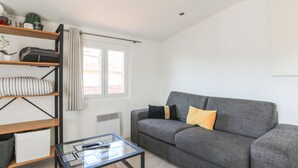 A modern living room with a grey sofa, a glass coffee table, and a wooden bookshelf. - Studio de la Buffa - Welkeys (Nice)