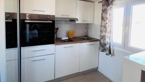 A compact kitchen with white cabinets, a built-in oven, a sink, and a window with floral curtains. - Studio de la Buffa - Welkeys (Nice)