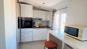 A compact kitchen with white cabinets, a built-in oven, a microwave, and two stools. - Studio de la Buffa - Welkeys (Nice)