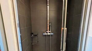 A shower with a handheld showerhead, a glass door, and a white sink with a bottle of hand soap. - Studio de la Buffa - Welkeys (Nice)
