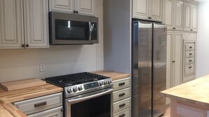 Eine moderne Küche mit Edelstahlherd, Mikrowelle und Kühlschrank, hellgrauen Schränken und einer Holz Arbeitsplatte.