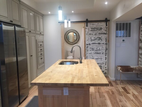 A kitchen with a central island, stainless steel refrigerator, and wooden flooring.