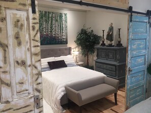 A bedroom with a bed, a nightstand, a dresser, a large plant, and a blue door.