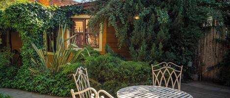 Un patio con sillas y mesa de metal, rodeado de abundante vegetación y una valla de madera.