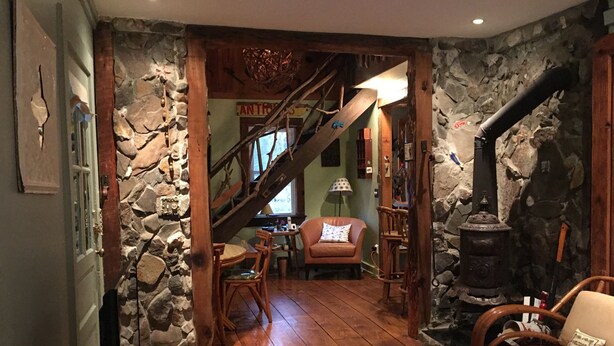 A cozy room with a stone wall, wooden floor, a staircase, a fireplace, and a comfortable chair.