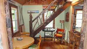 A rustic dining area with a wooden table and chairs, a staircase, and a view of the outdoors.