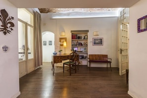 Une pièce avec un plancher en bois, un bureau avec une chaise, une bibliothèque, un canapé et une porte avec un miroir.