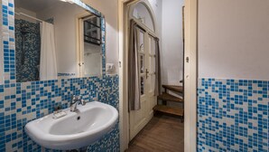 Ein Badezimmer mit einem weißen Waschbecken, blauen Mosaikfliesen, einer Holztür und einem Spiegel.