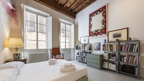 A bedroom with a bed, a chair, a bookshelf, a radiator, and a window.