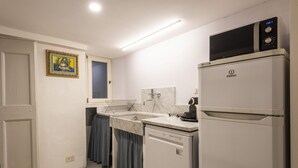 A compact kitchen with a refrigerator, microwave, and a sink with a marble countertop.