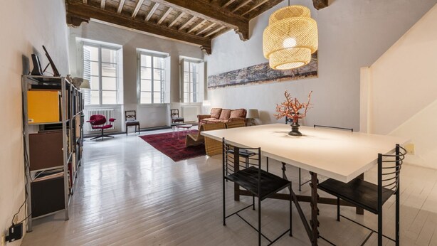 A spacious room with a large dining table, wooden beams on the ceiling, and a hanging light fixture.