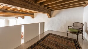 A room with exposed wooden beams, a patterned rug, and a chair with a cushion.