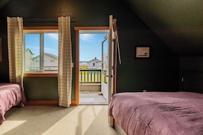 A bedroom with two beds, a window with curtains, and a view of a balcony and houses outside. - The Atlas - Sauna and Beach Access (Dr)