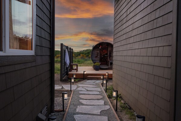 Un chemin de pierres menant à une terrasse en bois d’où l’on peut admirer un coucher de soleil.