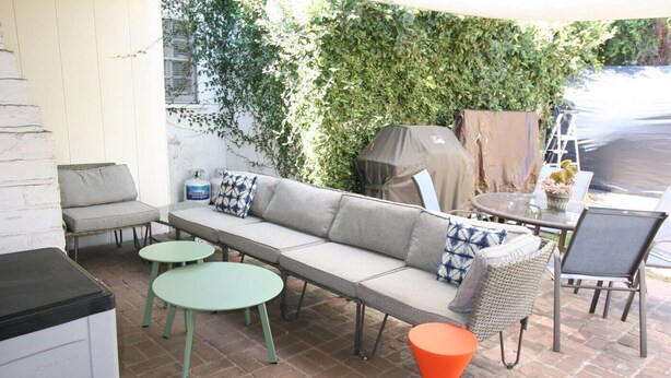 Eine Außenpatio mit einer Couch, zwei runden Tischen und einem Sessel.