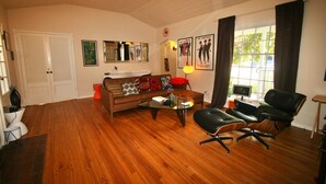 Ein Wohnzimmer mit Holzboden, einem braunen Sofa, einem schwarzen Ledersessel, einem Glastisch und einem Fenster mit Vorhängen.