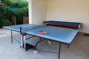 Enjoy a game of ping pong in our outdoor recreation area, featuring a pool table and lush garden surroundings.