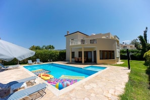 Ein zweigeschossiges Haus mit Swimmingpool, Liegestühlen und einer überdachten Terrasse.