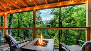 Une terrasse couverte avec un foyer, des sièges et une vue sur une forêt.