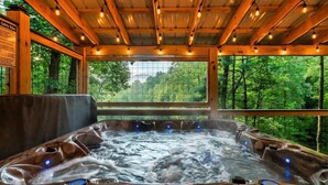 Un bain à remous avec un plafond en bois et une vue sur une forêt.
