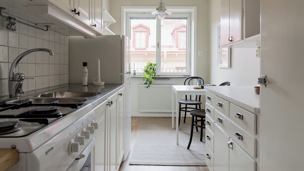 Une cuisine avec des meubles blancs, un fourneau et une fenêtre donnant sur des immeubles.