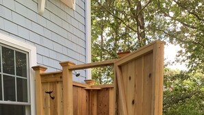 A wooden outdoor shower structure with a door, a small step, and a wooden bench.