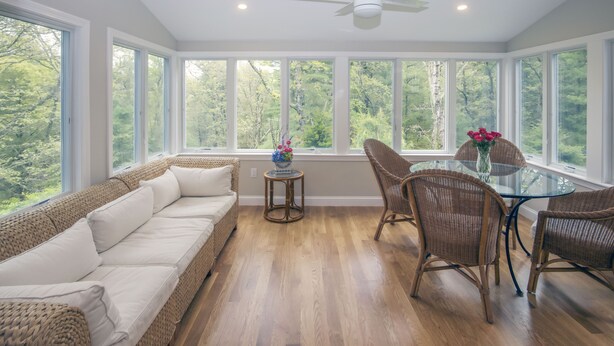 A sunroom with a large glass door, wicker furniture, and a ceiling fan.
