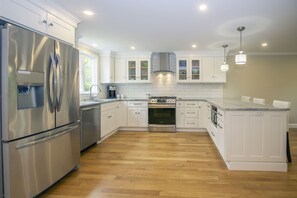 Una cocina moderna con electrodomésticos de acero inoxidable, armarios blancos y piso de madera.