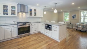 A modern kitchen with white cabinetry, stainless steel appliances, and a wooden floor.