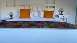 A bed with a white headboard, two orange pillows, and a colorful quilt. There is a white nightstand with a lamp and a small table with a lamp on it. - Family Cottage With Pool and Spectacular Views in a Rural Setting (Velez-Malaga)