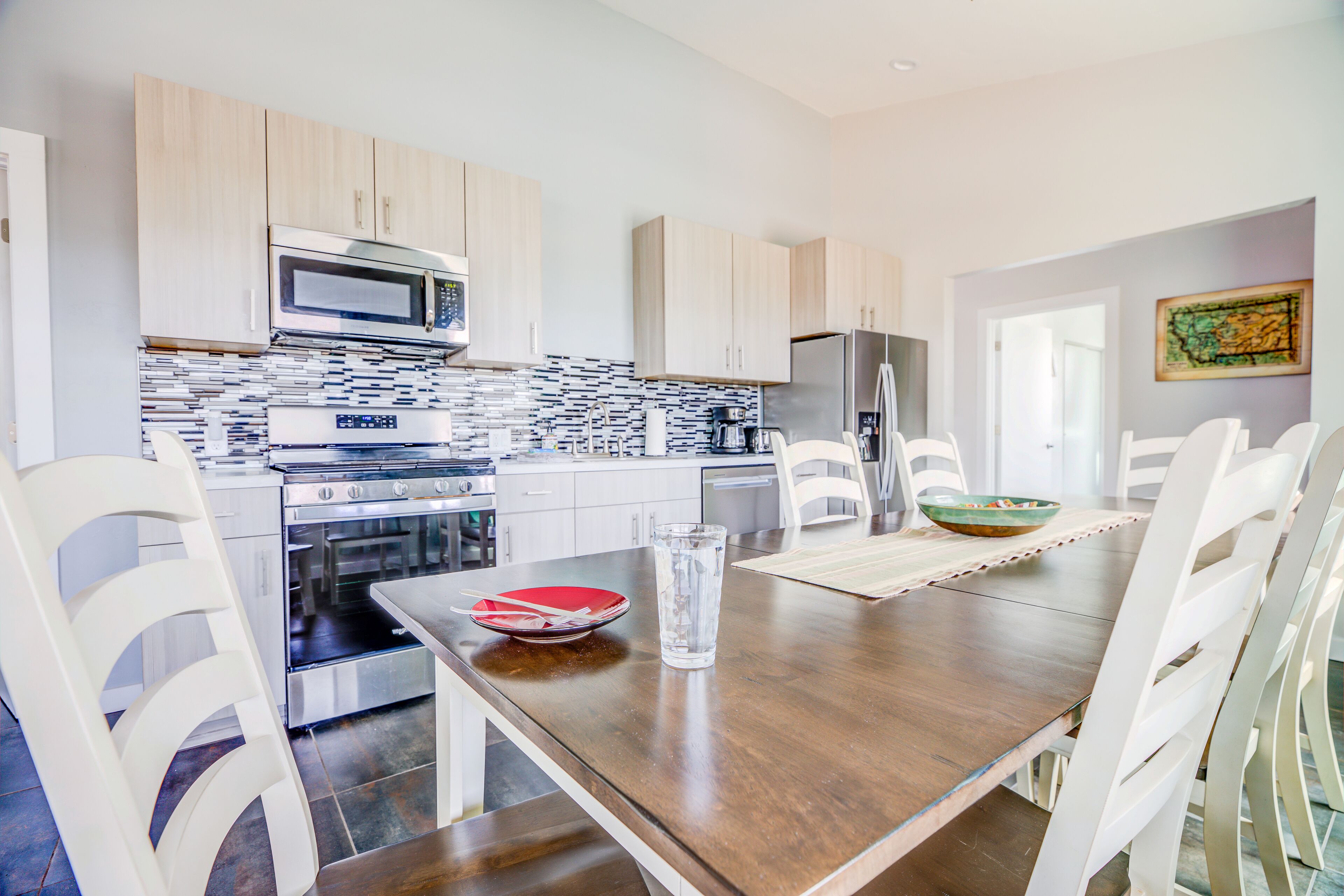 Una cocina moderna con electrodomésticos de acero inoxidable, armarios blancos y un comedor con mesa de madera y sillas blancas.