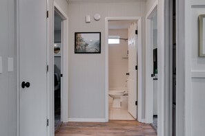 Een gang die leidt naar een badkamer met een toilet, een douche en een inlijsting foto aan de muur.