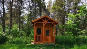 Uma cabana de madeira com varanda, rodeada por uma floresta densa.