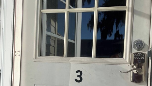 Una puerta blanca con el número 3, una ventana y una cerradura electrónica.