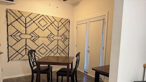 Un comedor con una mesa y sillas de madera, un tapete tejido grande en la pared y una puerta con perchero para toallas.