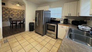 Una cocina compacta con armarios blancos, un refrigerador de acero inoxidable, un horno, un fregadero y una zona de comedor con mesa y sillas.