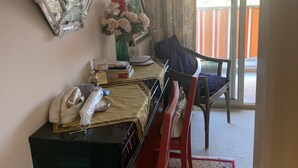 Ein Zimmer mit Schreibtisch, Stühlen, einem Spiegel, einer Vase mit Blumen und Blick durch ein Fenster mit Vorhängen.