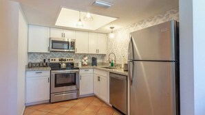 Cozinha moderna com armários brancos, eletrodomésticos de aço inoxidável e piso cerâmico.