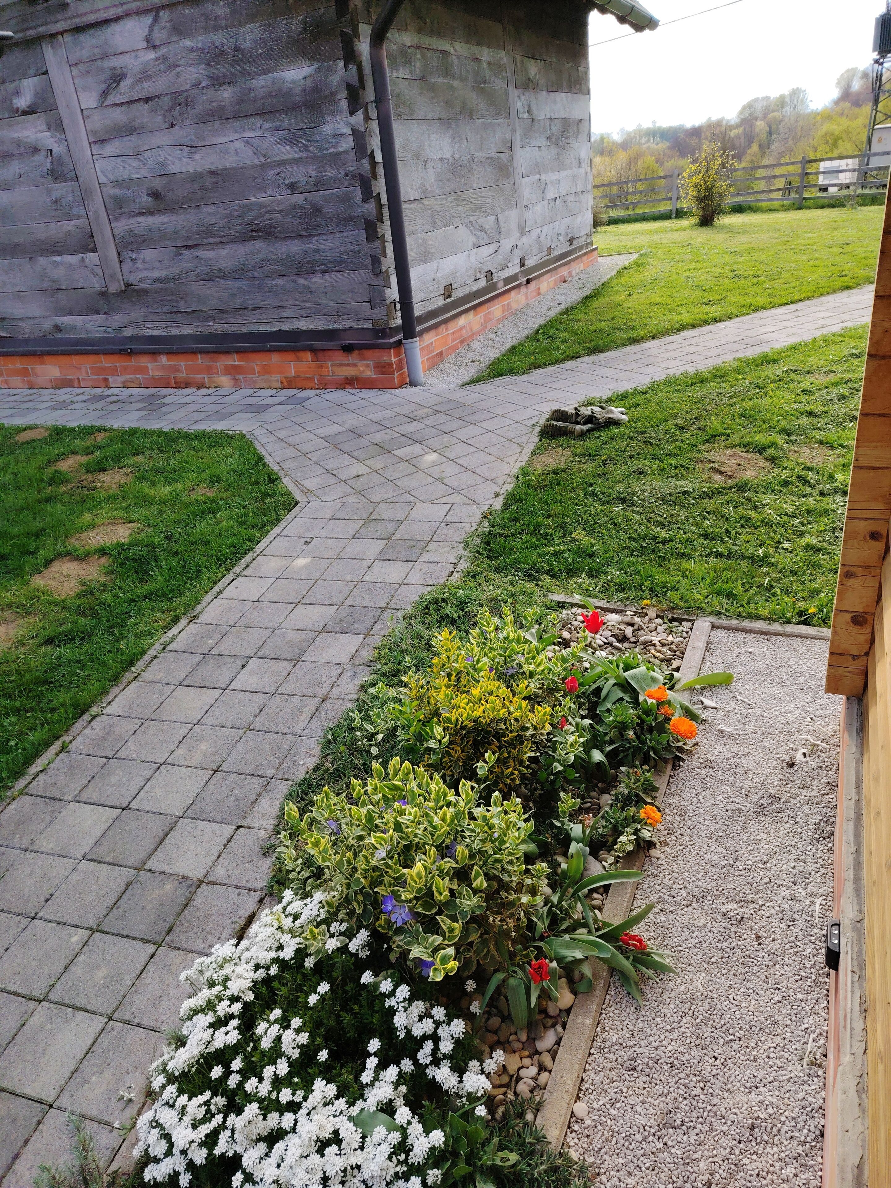 Un sentier de jardin mène à un bâtiment en bois dont les fondations sont en briques.