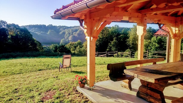 Un quiosco de madera con un banco y una silla, con vista a un campo cubierto de césped y vistas de colinas y árboles.