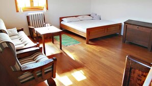 Una habitación con cama, cómoda de madera, una silla a rayas, una mesita y una ventana con cortinas.